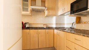 Een keuken met houten kastjes, een granieten aanrecht, een roestvrijstalen spoelbak en een zwarte magnetron.