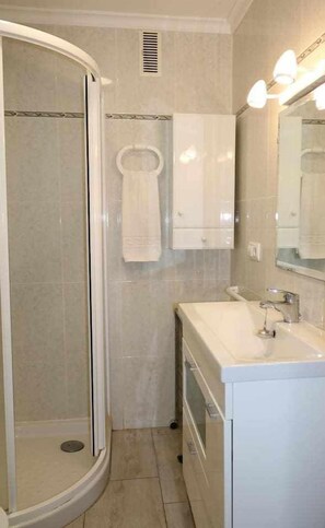 Een badkamer met douche, wastafel, spiegel en handdoekhouder.