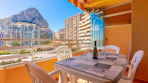 A balcony with a table, chairs, a bottle of wine, and a glass. In the background, there are high-rise buildings and a mountain. - 25D Voramar, 2-Bedroom (Calpe/Calp)