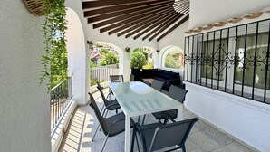 Un patio cubierto con mesa y sillas, una planta colgante y vistas del barrio circundante.