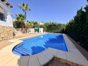 Ein Swimmingpool mit einer Steinmauer und Palmen, umgeben von einem Zaun.