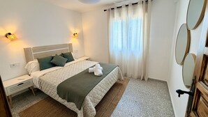 Un dormitorio con cama, mesitas de noche, ventilador de techo y una ventana con cortinas.
