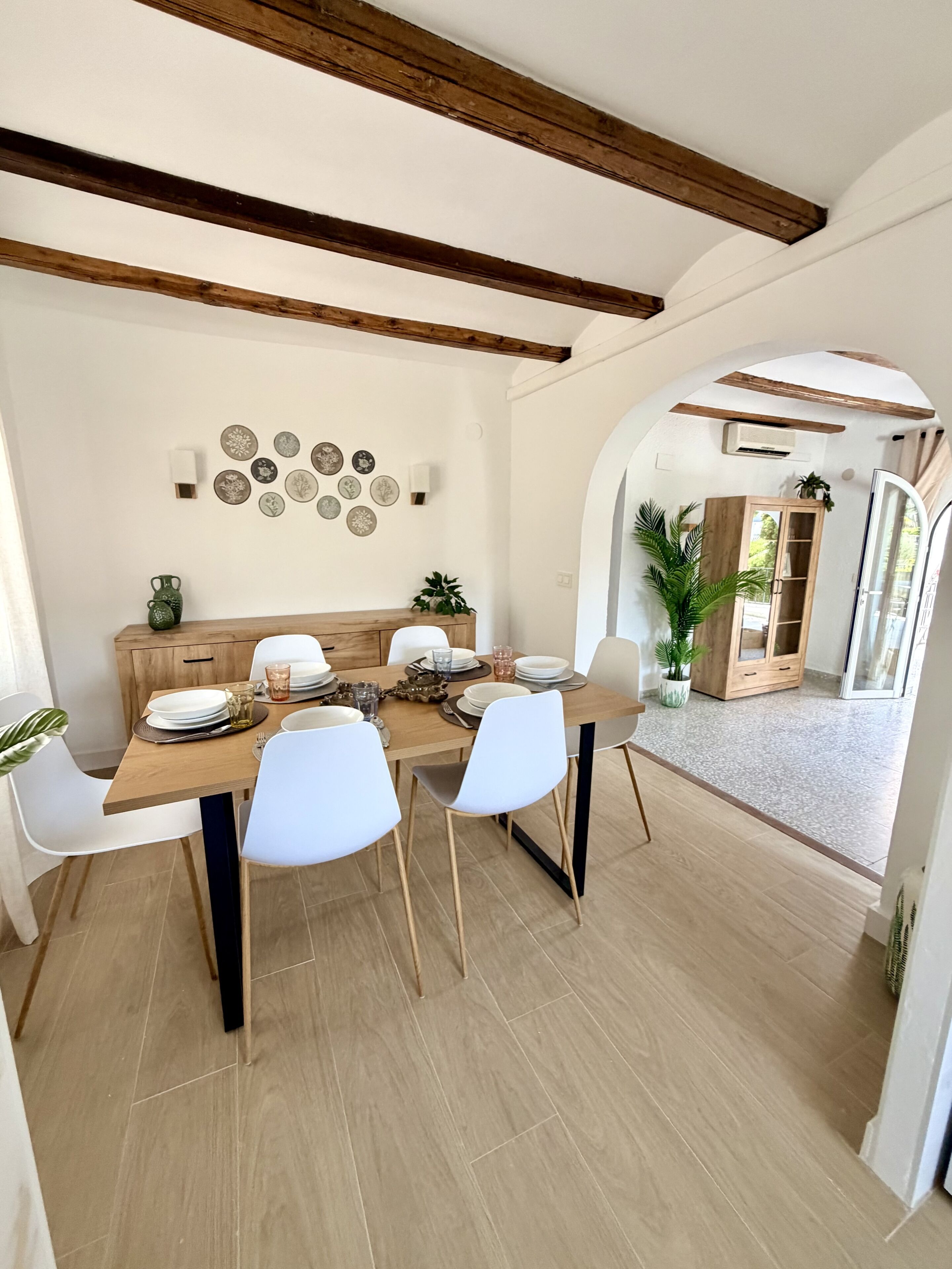 A dining area with a wooden table, white chairs, and a wall decorated with plates.