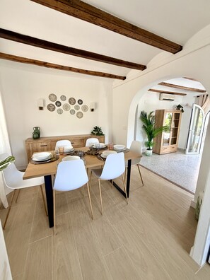 Un comedor con una mesa de madera, sillas blancas y una pared decorada con platos.