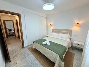 Ein Hotelzimmer mit einem Bett, einem Nachttisch, einer Wandlampe und einer Tür zu einem anderen Raum.