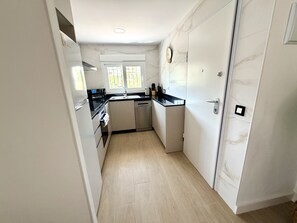 Een smalle keuken met witte kastjes, een zwart aanrecht en een ingebouwde oven.