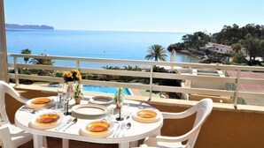 A dining table set with plates, cutlery, and glasses, overlooking a pool and a scenic view of the sea and hills.