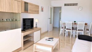 A modern living room with a TV, a small table, and a dining area with chairs.
