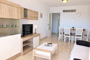Uma sala de estar moderna com televisão, uma mesinha e um espaço de jantar com cadeiras.
