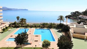 A hotel with a pool area, palm trees, and a view of the sea.