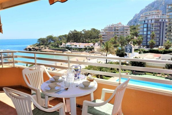 A balcony with a table set for dining, overlooking a beach and a mountainous landscape. - 14B Vora 1st line of the beach with sea views (Calpe/Calp)
