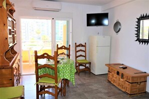 A compact kitchen with a dining area, a TV mounted on the wall, and a refrigerator. - 14B Vora 1st line of the beach with sea views (Calpe/Calp)