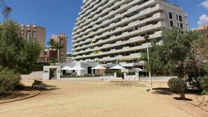 A multi-story hotel with a modern design, featuring balconies on each floor, a central courtyard with outdoor seating, and a parking area in front. - 112 Calpeplace with large terrace, wifi and pool (Calpe/Calp)