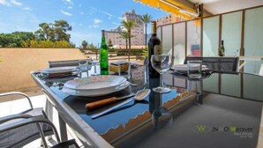 A dining area with a table set for two, a bottle of wine, and a glass. The table is near a window with a view of a building and trees. - 112 Calpeplace with large terrace, wifi and pool (Calpe/Calp)