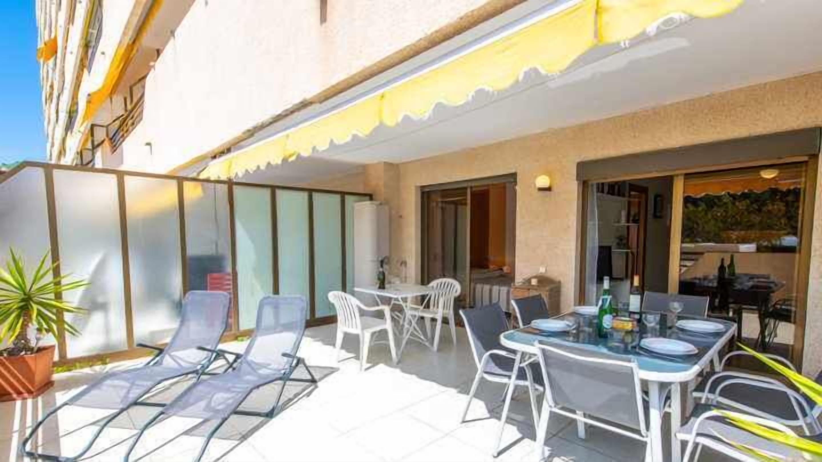 An outdoor patio with sun loungers, a table with chairs, and a glass balustrade.