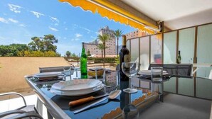 Un coin repas avec une table dressée pour deux personnes, une bouteille de vin et un verre. La table est placée près d’une fenêtre d’où l’on peut admirer un bâtiment et des arbres.