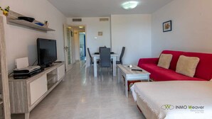 A hotel room with a TV, a red sofa, a dining table with chairs, and a kitchen area in the background. - 13D TB 2 bedrooms, 2nd line beach with sea views (Calpe/Calp)