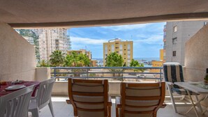 A balcony with two wooden chairs and a table, overlooking a coastal area with buildings and a clear sky. - 13D TB 2 bedrooms, 2nd line beach with sea views (Calpe/Calp)
