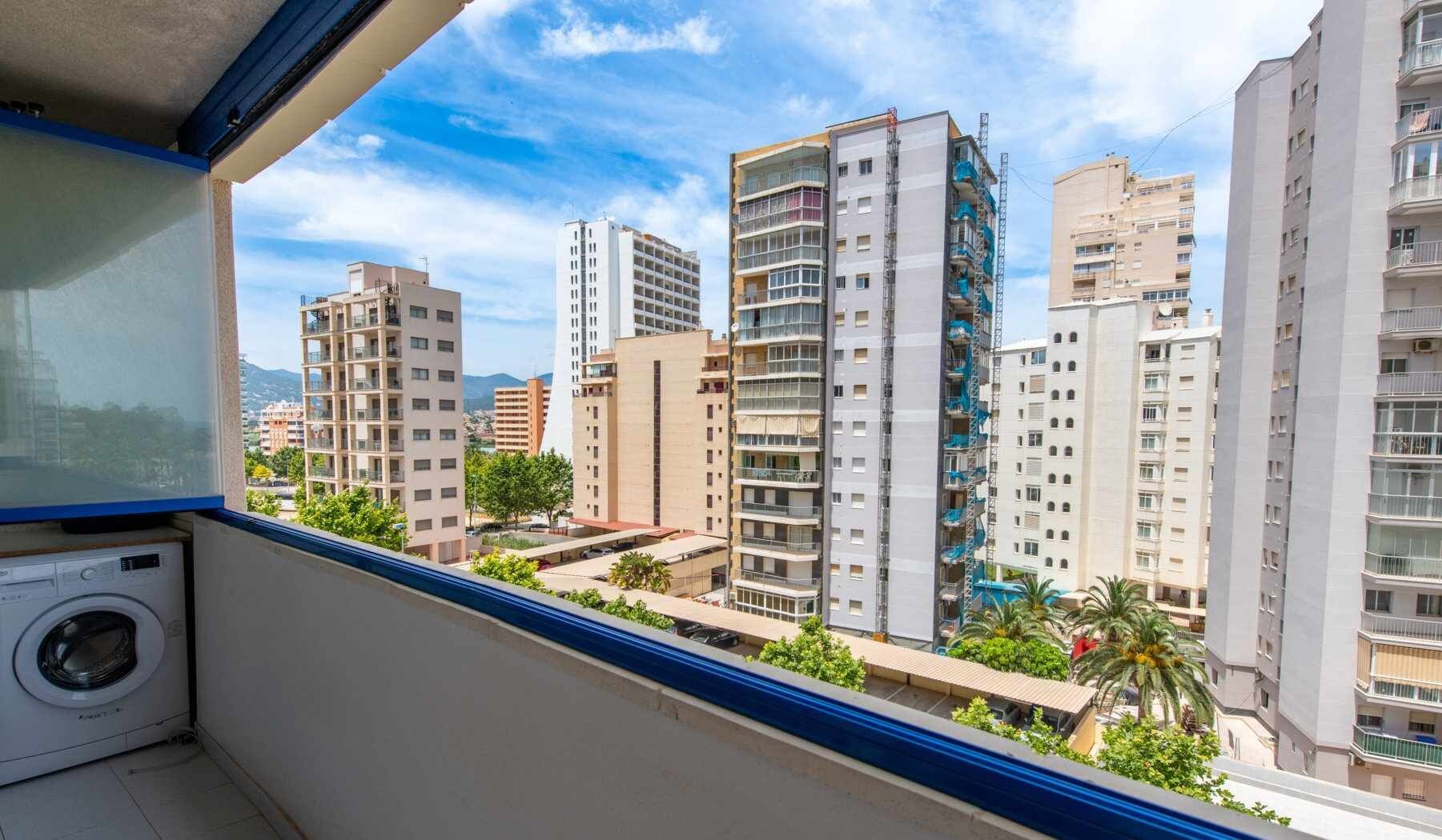 Ein Balkon mit Blick auf hohe Wohngebäude, einer Waschmaschine und einem wolkenlosen Himmel.