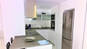 Une cuisine compacte avec un coin repas, des meubles blancs, un réfrigérateur en acier inoxydable et un four à micro-ondes.