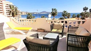 Une terrasse sur le toit, dotée de chaises longues jaunes, de meubles en osier et offrant une vue sur la mer et les montagnes.