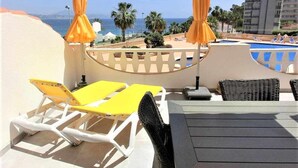 Une terrasse avec des fauteuils de jardin jaunes, une table et une vue sur la mer et les bâtiments.