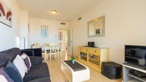 A living room with a sofa, coffee table, TV, bookshelf, and a dining area with chairs and a table. - Apollo17 E39, 2 bedrooms (Calpe/Calp)