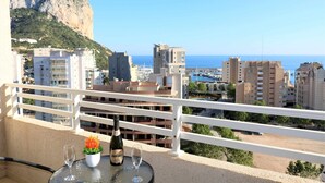 A balcony with a table, a bottle of champagne, and a glass, overlooking a coastal cityscape with buildings and a mountain. - Apollo17 E39, 2 bedrooms (Calpe/Calp)