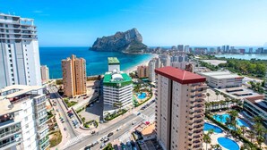 Un paisaje costero con rascacielos, una isla rocosa destacada y un cielo azul despejado.