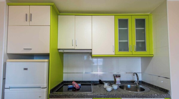 Uma cozinha compacta com armários brancos e verde-lima, uma pia de aço inoxidável e um fogão embutido.