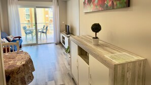 A modern living room with a sofa, a dining table, a TV, and a balcony with a view of buildings.