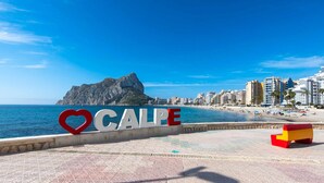 A coastal cityscape with a prominent rock formation, a beach, and a 'Calle' sign.