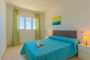 A bedroom with a bed, a window with curtains, a bedside table with a lamp, and a wall painting. - APOLLO17 E37, 3 bedrooms (Calpe/Calp)