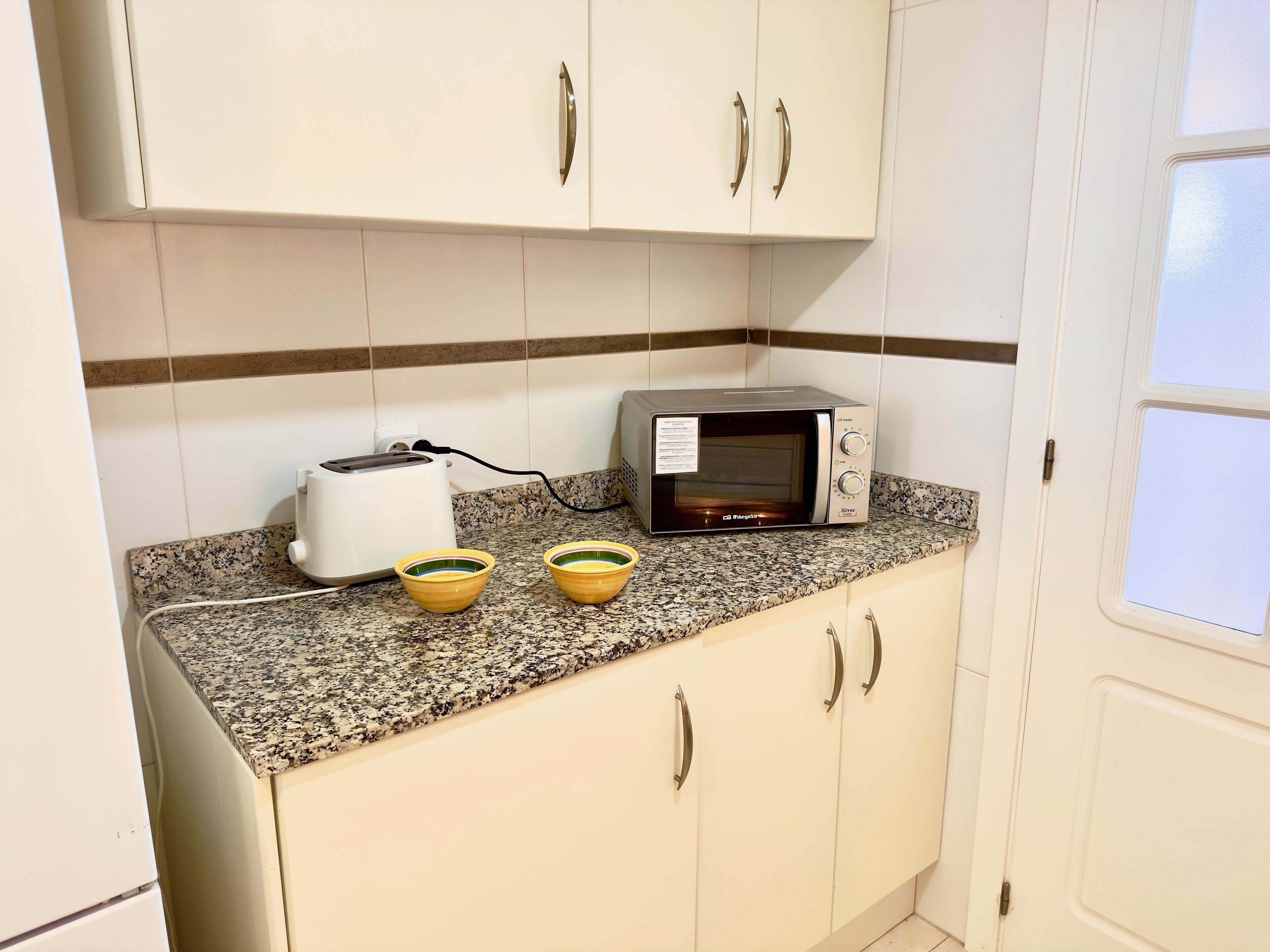 A kitchen with white cabinets, a granite countertop, a toaster, a microwave, and two yellow bowls.