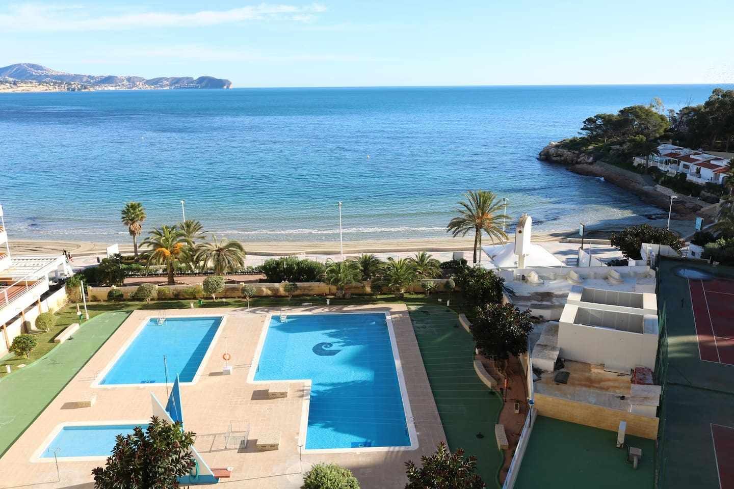A resort with two swimming pools, a beach, and a view of the sea.