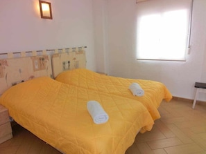 Ein Zimmer mit zwei Betten, jedes mit einer gelben Tagesdecke und zusammengerollten Handtüchern.