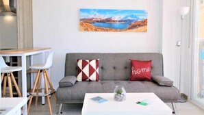 Ein modernes Wohnzimmer mit einem grauen Sofa, zwei Sesseln, einem Couchtisch und einem Landschaftsbild.
