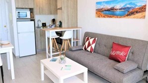 Ein kompakter Wohnraum mit Küchenzeile, einer Couch mit Zierkissen und einem Gemälde einer Berglandschaft.