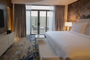 Een hotelkamer met een groot bed, een bank, een televisie, een bureau en een balkon met een stoel.