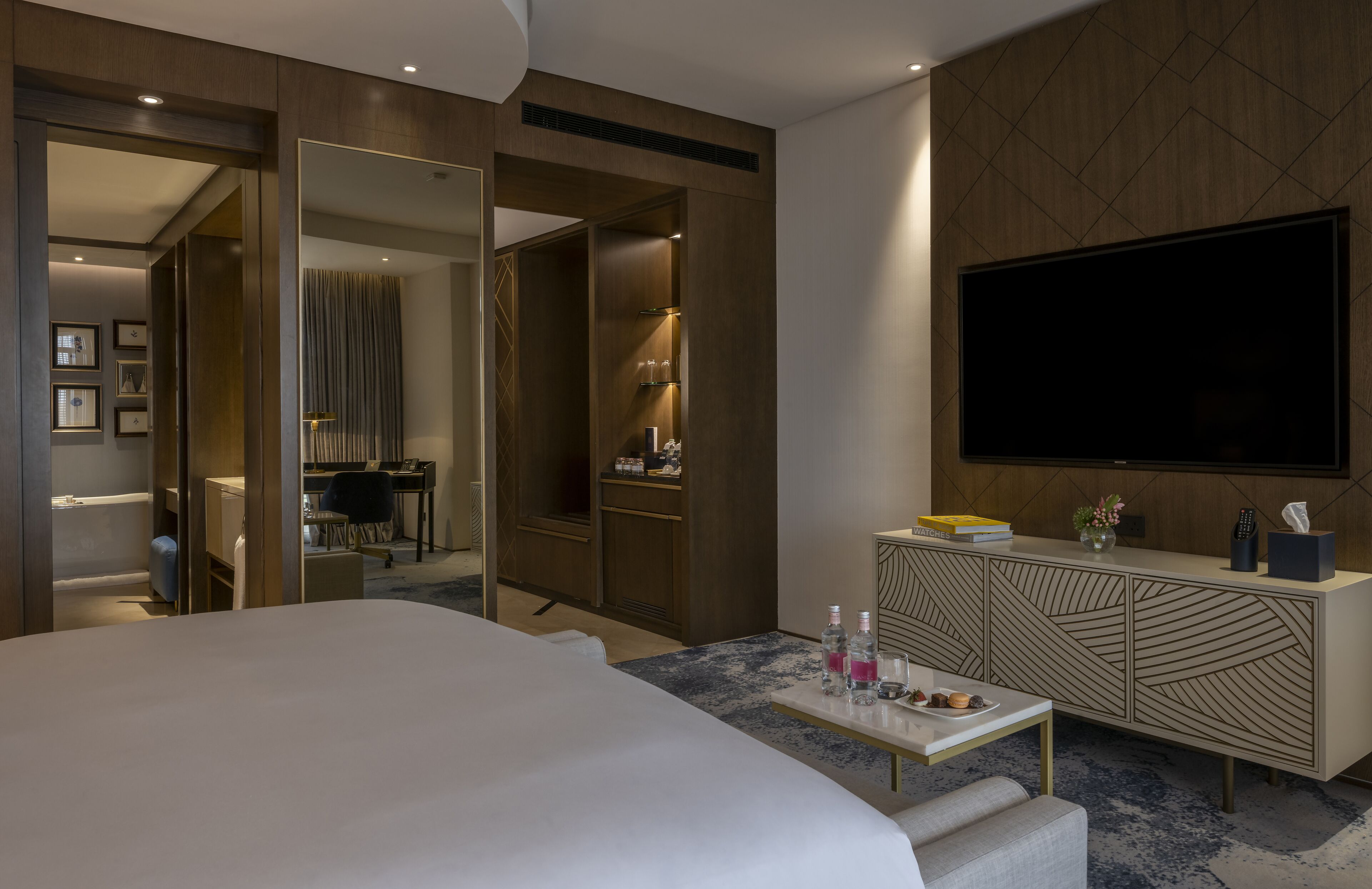 Una habitación de hotel moderna con una cama grande, un televisor de pantalla plana, un minibar y un vestidor.