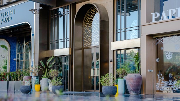 Un edificio moderno con amplios ventanales, un arco central y plantas en macetas al frente.
