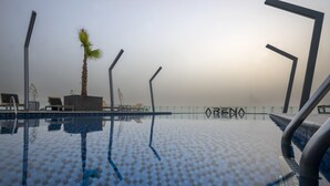Una piscina con baldosas a cuadros, sillas de descanso y una palmera.