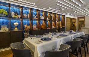 Een eetgedeelte met gedekte tafels, een decoratieve wand met blauwe tegels en een modern plafondontwerp.