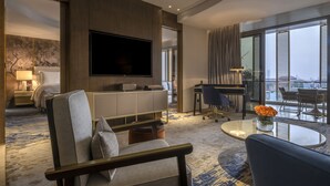 Habitación de hotel moderna con televisor grande, asientos cómodos, escritorio y balcón con vistas.