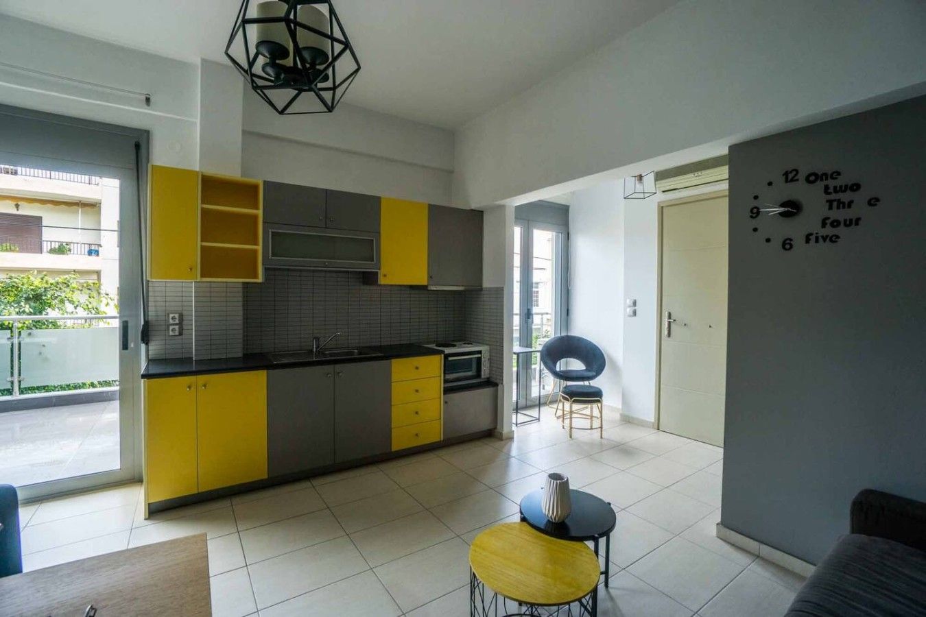 Une cuisine moderne avec des meubles de couleur jaune et grise, un plan de travail noir et un coin repas comprenant une chaise jaune et une petite table.