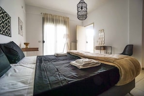 Un dormitorio con cama, mesita de noche, lámpara y una silla.