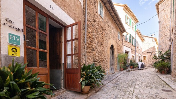 A narrow cobblestone street with stone buildings, a wooden door, and potted plants. - L'Angel by Rentallorca (Biniaraix)