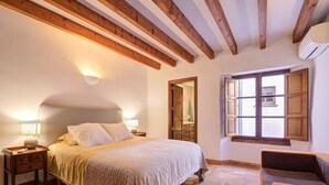 A bedroom with a large bed, wooden beams on the ceiling, a nightstand, a chair, and a window with wooden shutters. - L'Angel by Rentallorca (Biniaraix)