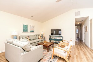 A living room with a sofa, armchair, coffee table, and a television on a stand.