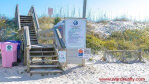 A wooden staircase leading to beach access, with a sign indicating beach rules and a trash can nearby.